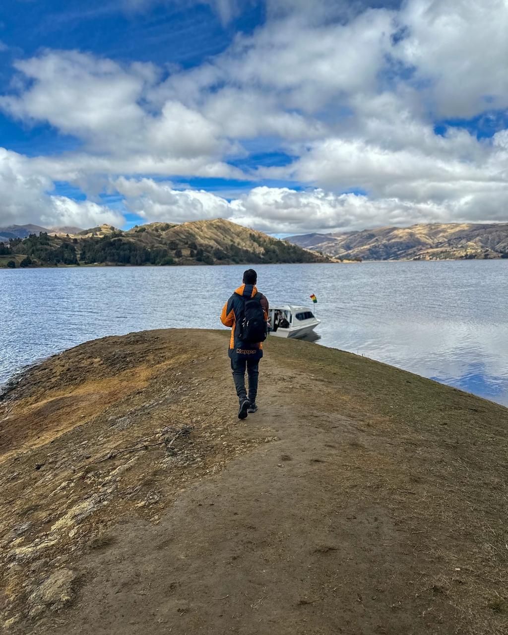 Walking out along a spit of land toward a lake in the Bolivian highlands, a small boat moored at the end of it.